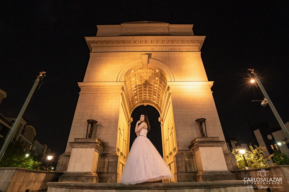 Elegant woman in a gown posing under the arch of a grand monument at night